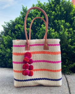 a medium woven straw bag with orange and pink stripes, and a pink pom pom attachment on the handle