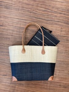 A navy and cream block striped Shebobo bag is lying on the wood floor with a navy and white pinstriped makeup bag placed inside it.