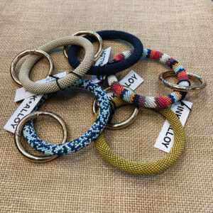 five beaded key rings arranged in a circle - clockwise from the top middle: navy; pink, maroon, navy, white, blue, purple, and yellow stripes; mustard yellow; light and dark blue speckles; beige