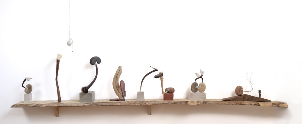 8 small sculptures made of wood, metal, and stone spaced horizontally on a live-edge wooden shelf