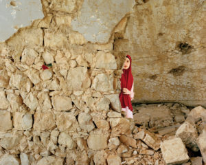Mariam from Lebanon peeking around the corner of a crumbling stone wall