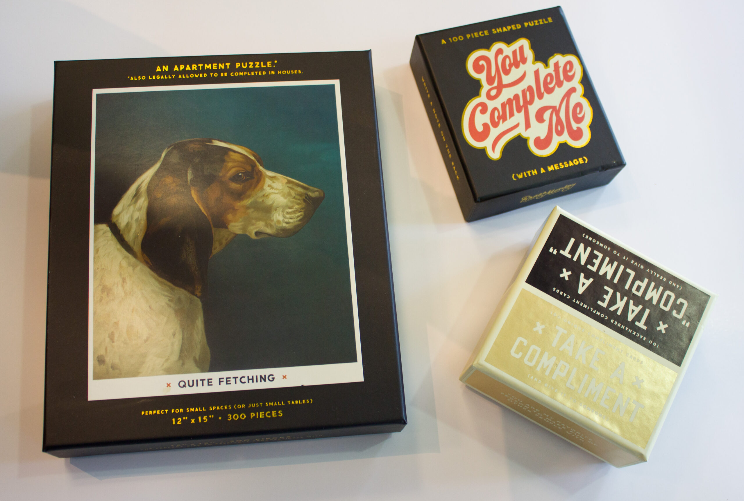 a close-up of the previous collection: a dog puzzle, a mini puzzle, and a compliments card game